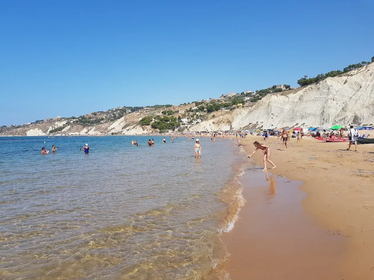Bambini giocano e bagnanti si godono il sole sulla spiaggia di marianello licata, con le bianche scogliere a fare da sfondo.