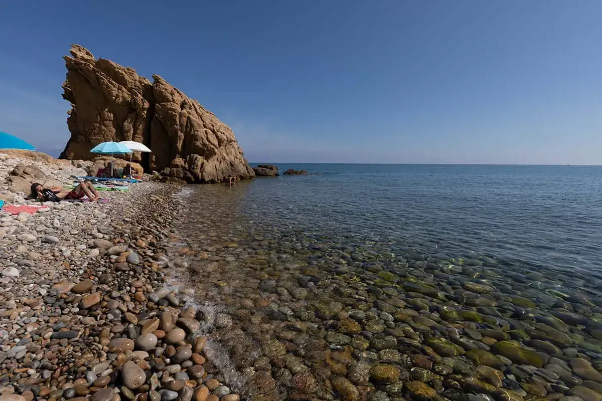 Spiaggia di ciottoli con scogliera imponente e mare cristallino. Un angolo di paradiso a Lampare Tusa, ideale per rilassarsi al sole.