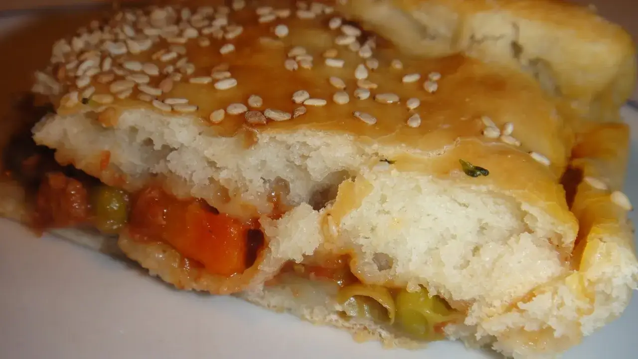 Fetta di brioscione palermitano con ripieno di verdure e semi di sesamo sulla crosta dorata.