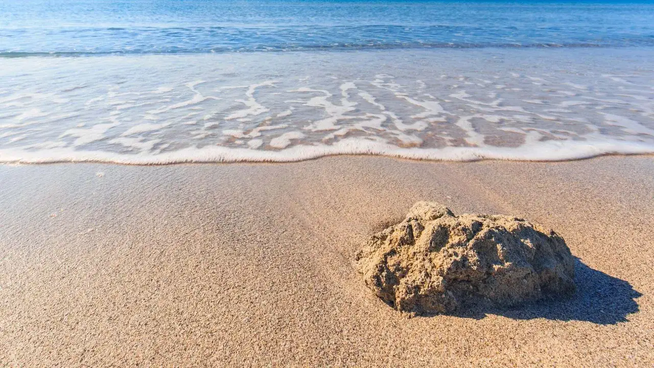 Sabbia dorata e mare calmo sulla spiaggia Tonnarella Mazara. Un sasso solitario osserva le onde che lambiscono la riva.