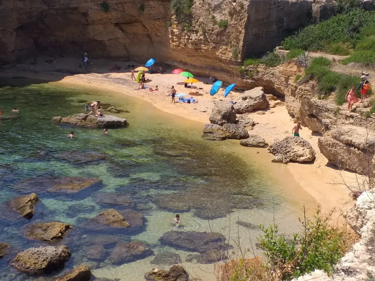 Bambini e adulti si godono il sole e il mare cristallino sulla spiaggia di Massolivieri, tra scogliere dorate e ombrelloni colorati.