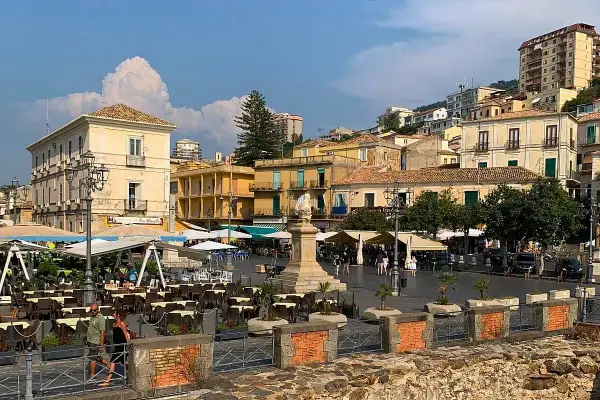 Piazza animata nel pizzo calabro centro storico, con tavoli all'aperto di ristoranti e palazzi storici sullo sfondo.