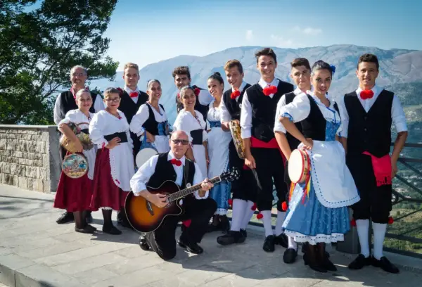 Un gruppo di persone in abiti tradizionali siciliani, pronti a intonare canzoni siciliane famose con chitarra e tamburello.