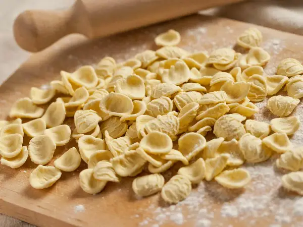 Orecchiette fresche, pronte per diventare uno dei **piatti tipici pugliesi** più amati. Un mattarello sullo sfondo evoca la tradizione.