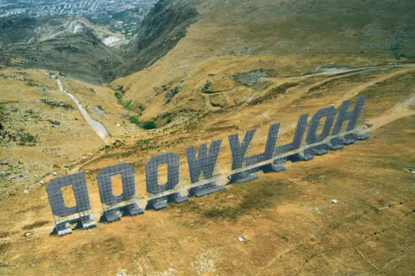 Aerial view of the "HOLLYWOOD" sign in Palermo, Italy, set against a dry, hilly landscape.