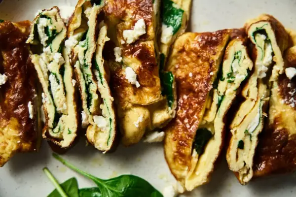 Rotoli di pisci d'ovu con spinaci e formaggio feta, dorati e invitanti, tagliati a fette per mostrare il ripieno cremoso.