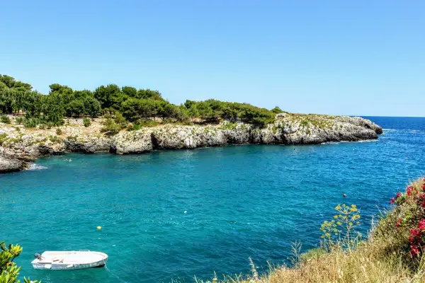 Acque cristalline e scogliere rocciose, un angolo di paradiso tra le spiagge Salento. Una piccola barca bianca galleggia tranquilla.
