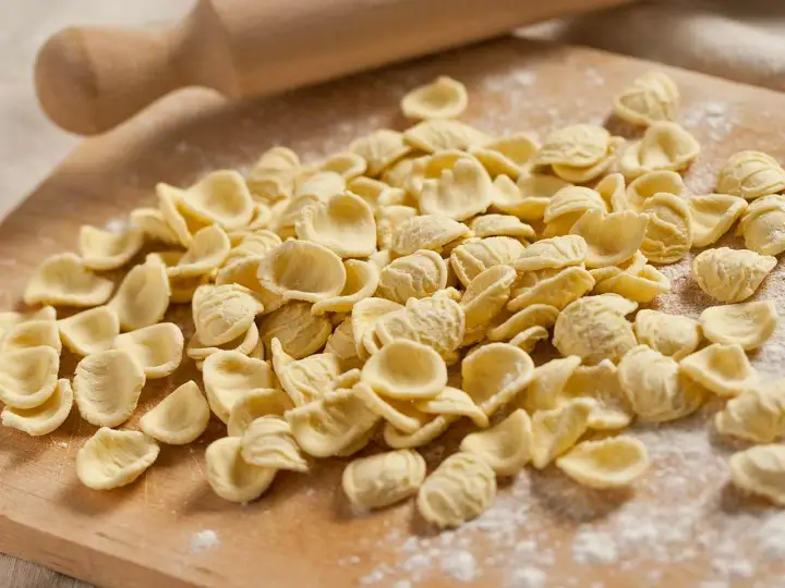 Orecchiette fresche, pronte per diventare uno dei **piatti tipici pugliesi** più amati. Un mattarello sullo sfondo evoca la tradizione.