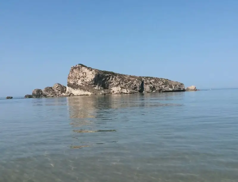 La Rocca San Nicola a Licata, imponente roccia calcarea che emerge dal mare cristallino, sotto un cielo azzurro.
