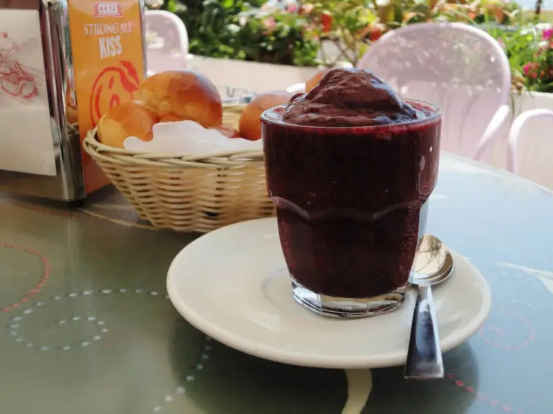 Un bicchiere di granita messinese, scura e invitante, accanto a soffici brioche in un cestino. Un'immagine che sa di sole e colazioni siciliane.