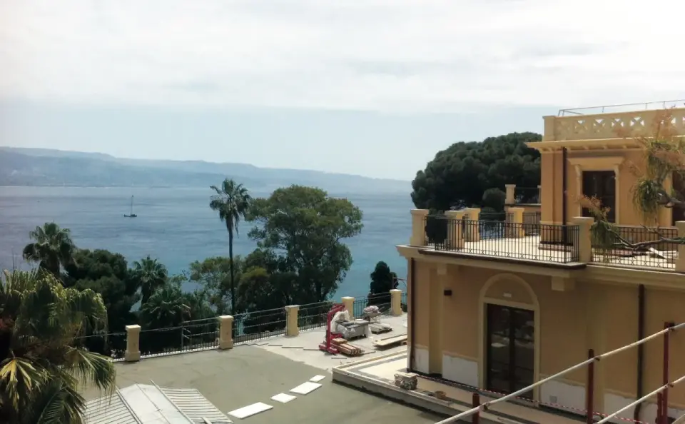 Vista mare dalla villa Bosurgi a Messina, con alberi tropicali e un veliero all'orizzonte.